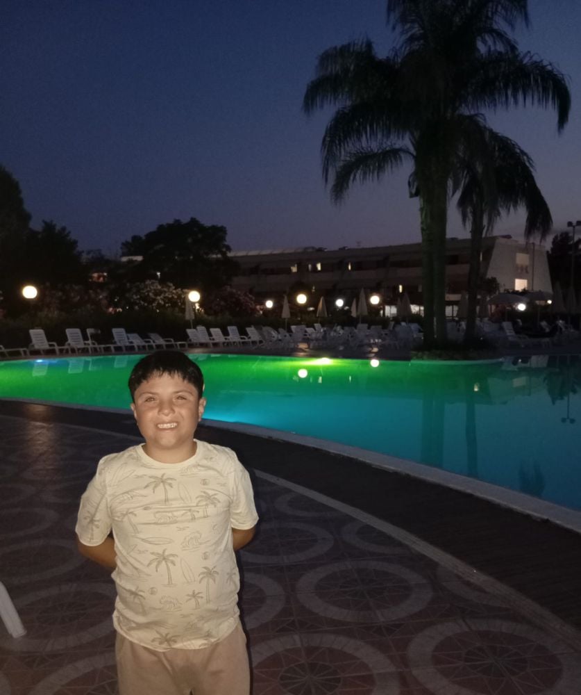 Bambino sorridente a bordo piscina, di sera
